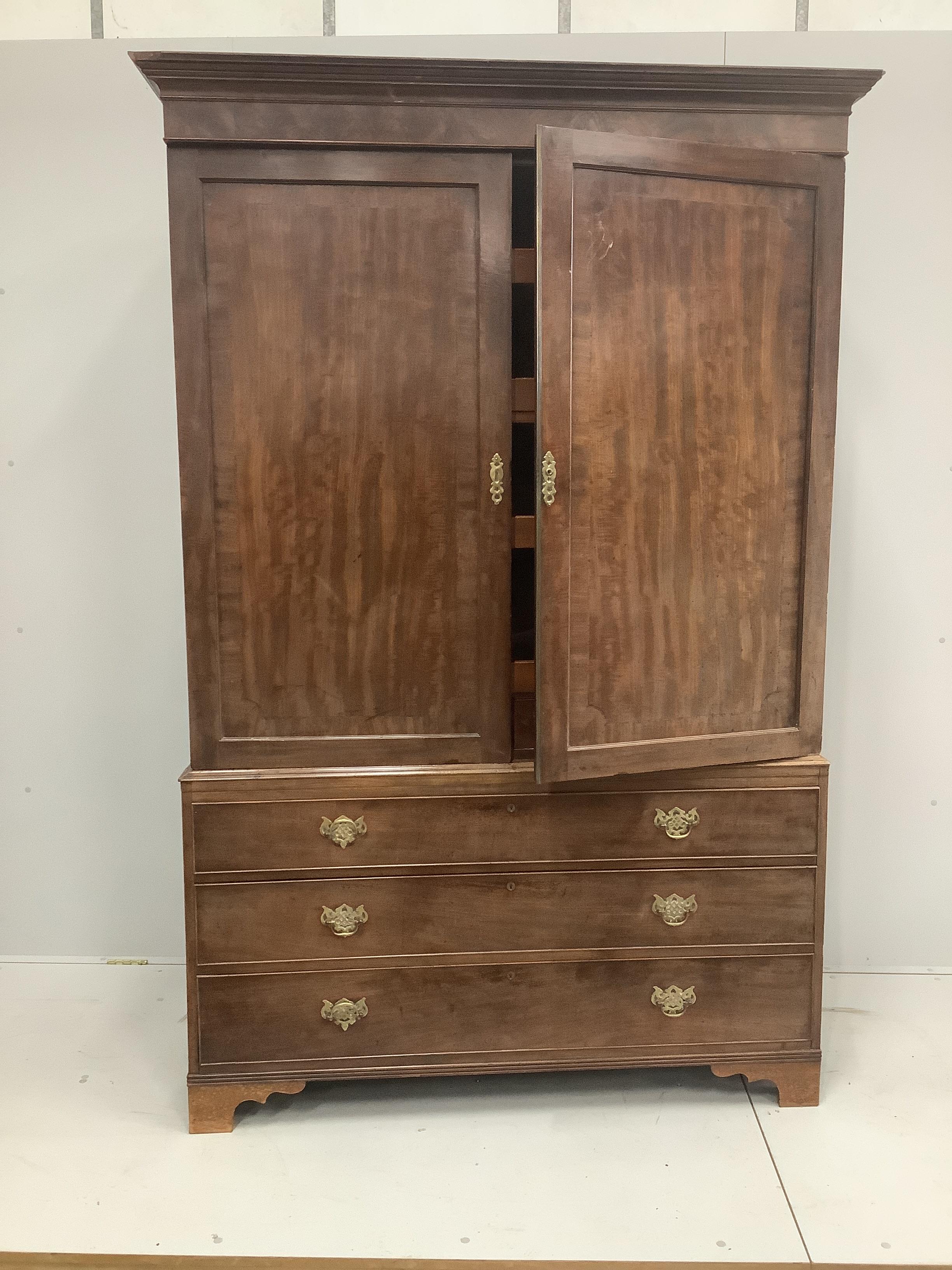 A George III mahogany linen press with moulded cornice and panelled doors enclosing sliding trays over three long drawers on bracket feet, width 137cm, height 195cm